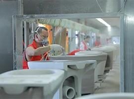 Worker spraying glaze on ceramic toilet units in a factory