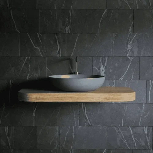 Minimalist bathroom with a floating wooden shelf, large gray sink, modern faucet, and dark marble tiled walls